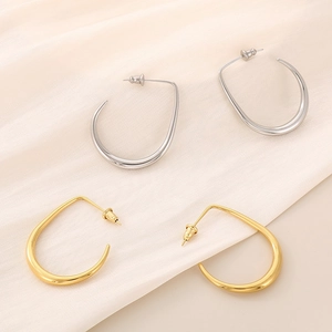 Detail of gold and silver U-shaped curved earrings on beige pleated silk fabric