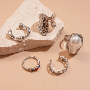 Five-piece silver geometric ring set with crystals and pearls on a stone surface