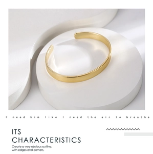 Detailed close-up of a minimalist gold-plated brass C-shaped open cuff on a white stand