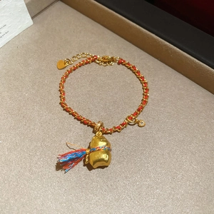 Dettaglio del bracciale placcato oro 24K con ciondolo a zucca, corda rossa e nappa colorata