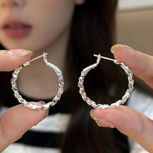Silver textured circle hoop earrings with faceted design held by hand in soft focus