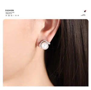 Close-up of a white pearl stud earring with a silver geometric base worn by a model