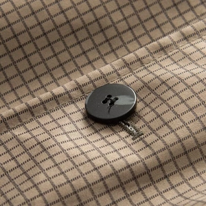 Macro detail of khaki checked fabric and a black resin button on a reversible coat