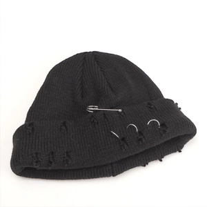 Macro shot of black ribbed knit beanie featuring punk metal rings and safety pin details