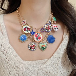 Detail of bohemian gold multi-charm necklace with colorful enamel heart and fruit pendants