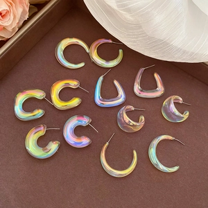 Detail of colorful holographic acrylic C-shaped earrings on a brown tray