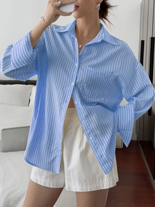 Detail of blue and white striped loose-fit long sleeve shirt in a cozy bedroom setting