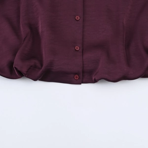 Detail view of the fuchsia satin blouse hemline and tonal buttons in a macro shot