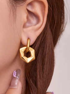 Close-up of gold geometric hexagonal drop earrings worn by a model with long brown hair