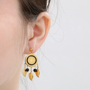Gros plan de boucles d'oreilles plumes dorées avec disque solaire et perles noires