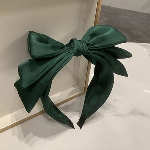 Detail of a dark green satin triple bow headband on a white marble background surface