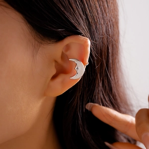 Macro shot of silver crescent moon face ear cuff on ear with metallic texture