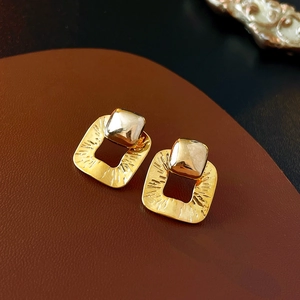 Macro detail of geometric hollow square earrings with radiant gold plated metal texture