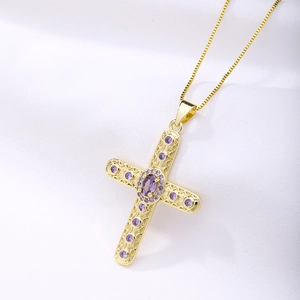 Close-up of gold cross pendant with purple oval zircon gemstone on silky fabric