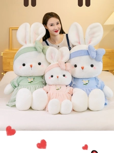 Detailed view of three soft plush rabbits in floral dresses held in a cozy bedroom setting
