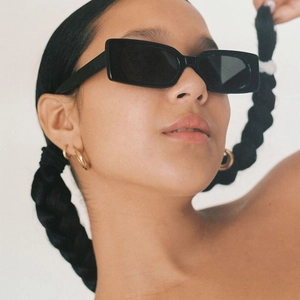 Close-up of stylish black square sunglasses and golden hoop earrings worn by a model
