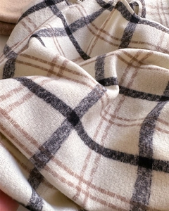 Close-up detail of soft beige plaid scarf with grey and brown woven texture and fringe