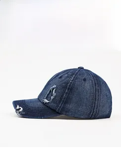 Detailed side view of distressed dark blue denim baseball cap with frayed hole design