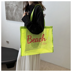 Detail of neon green mesh beach tote bag with red Beach Vibes text carried by a model