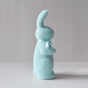 Side view of a light blue flocked Easter rabbit ornament with a matching ribbon bow