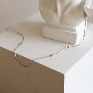Detail of silver snake chain necklace with small beads draped over white geometric decor