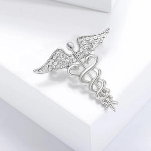 Detail view of silver Caduceus brooch featuring angel wings and crystal-set snakes