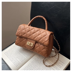 Close-up of brown quilted bag with gold chain strap and turn-lock on a book