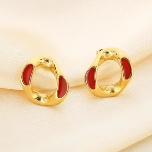 Macro shot of gold geometric earrings with red enamel on a silk background