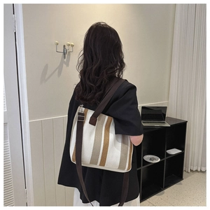 Detail showing vertical striped canvas tote bag worn by model in a cozy home setting