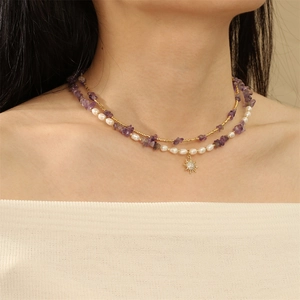 Close-up of layered necklace with purple stones, white pearls and gold sun pendant