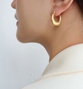 Gros plan d'une boucle d'oreille créole dorée style croissant avec détail en métal texturé