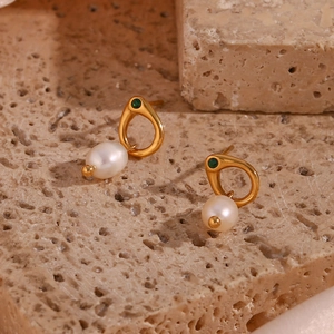 Detailed shot of gold earring with green gemstone and white pearl on stone background