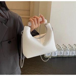 Detail of white textured leather bag featuring clear pearl handle and silver chain strap