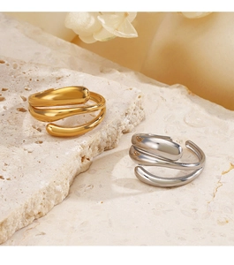 Dettaglio di anelli a spirale irregolari placcati oro 18K e argento su pietra beige