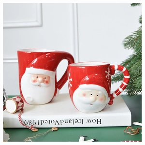 Detail of red Santa Claus ceramic mugs set displayed with Christmas pine on a green desk