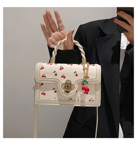 Detail of white leather handbag featuring red cherry prints and camellia metal clasp