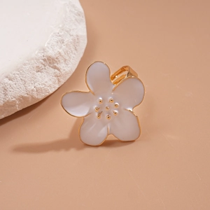 Détail d'une bague fleur en émail blanc avec accents dorés sur un support en pierre