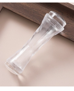 Close-up of double-ended clear silicone nail stamper with ergonomic handle on wooden frame