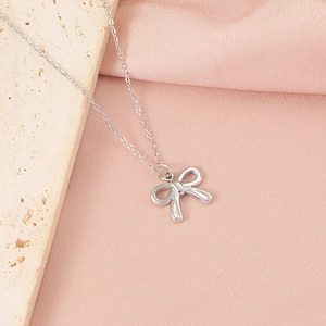Gros plan d'un collier pendentif nœud argenté sur pierre beige et soie rose