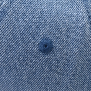Detail of embroidered eyelet and twill texture on washed blue denim baseball cap