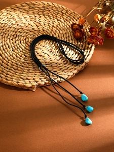 Detail of bohemian turquoise stone pendant necklace with black velvet rope on woven mat