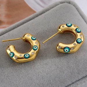 Macro shot of gold C-shaped earrings with enamel evil eye and white cubic zirconia