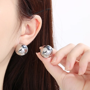Close-up of oversized silver ball earrings featuring a polished metallic finish on a model