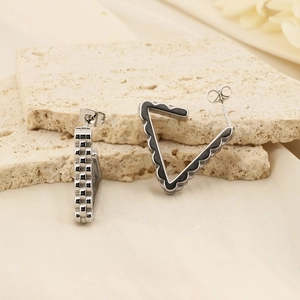 Macro view of geometric triangular earrings on beige stone texture background
