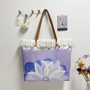 Detail of purple canvas tote bag with lotus print and white fringe tassels on a wall