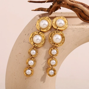 Détail de boucles d'oreilles pendantes avec perles blanches et texture en métal doré