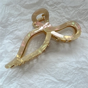 Close-up of cream acetate bow hair claw with elegant iridescent finish and gold hardware