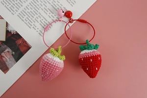 Detailed view of handmade crochet strawberry keychains in pink and red with small bells