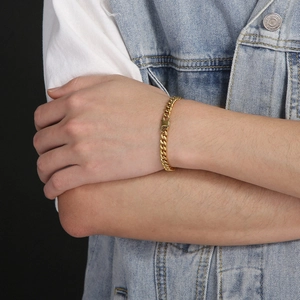 Detailed close-up of a gold Cuban link chain bracelet worn on a model's wrist