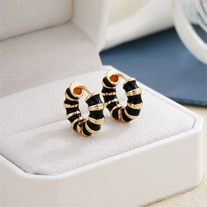 Macro shot of gold-plated hoop earrings with black enamel detail on white velvet box